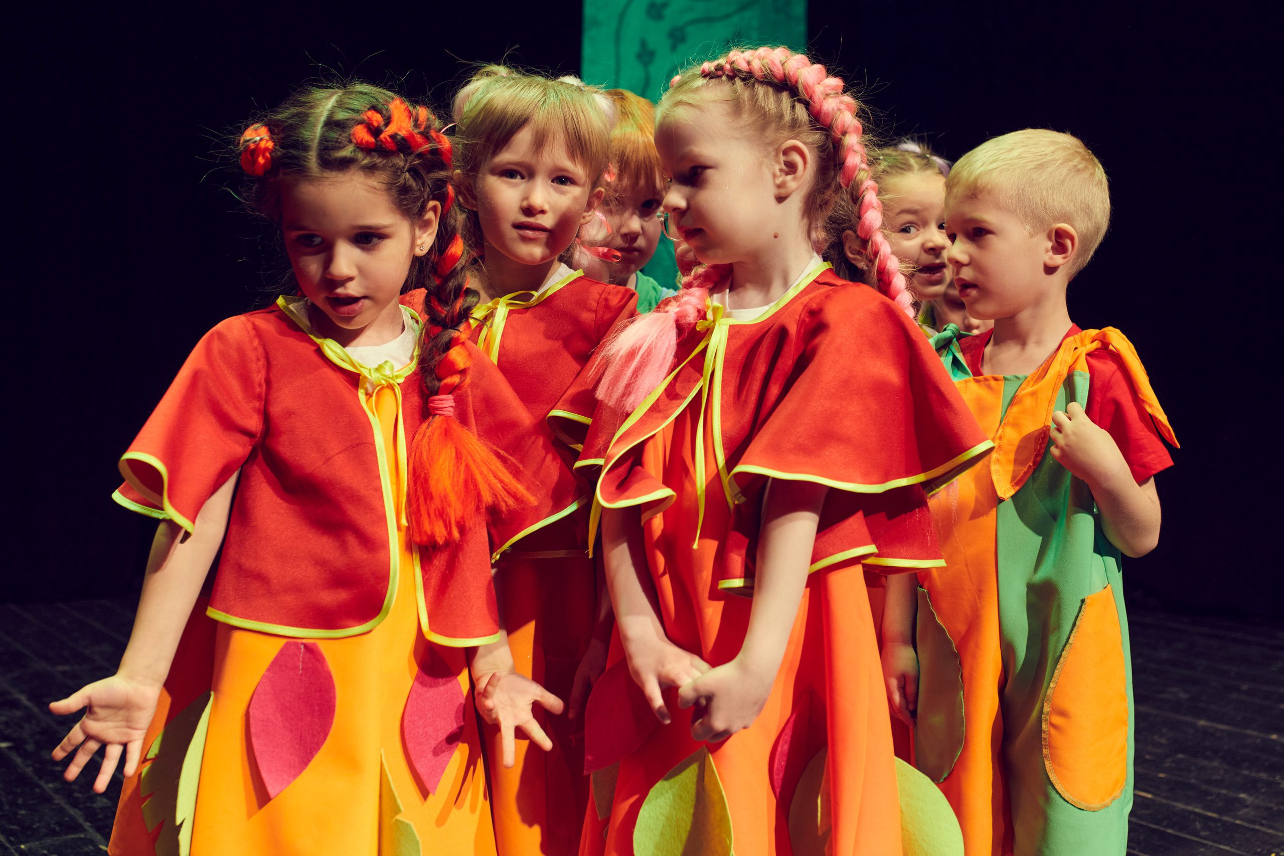 Маленькие дети лет 7 в в разноцветных костюмах, похожих на осенние листья играют на сцене театра