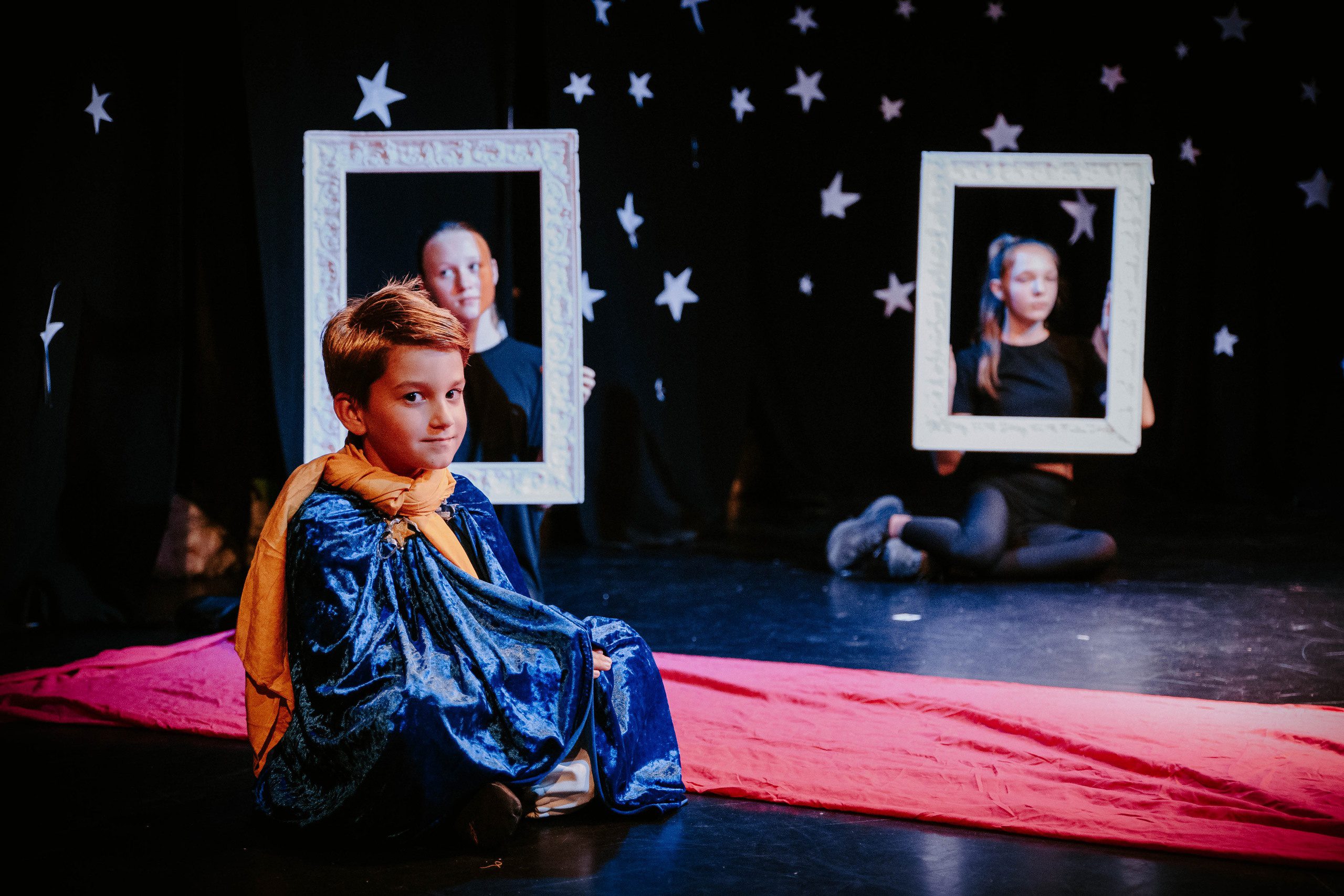 маленький мальчик облачившись в мантию сидит на фоне звездного неба в театре