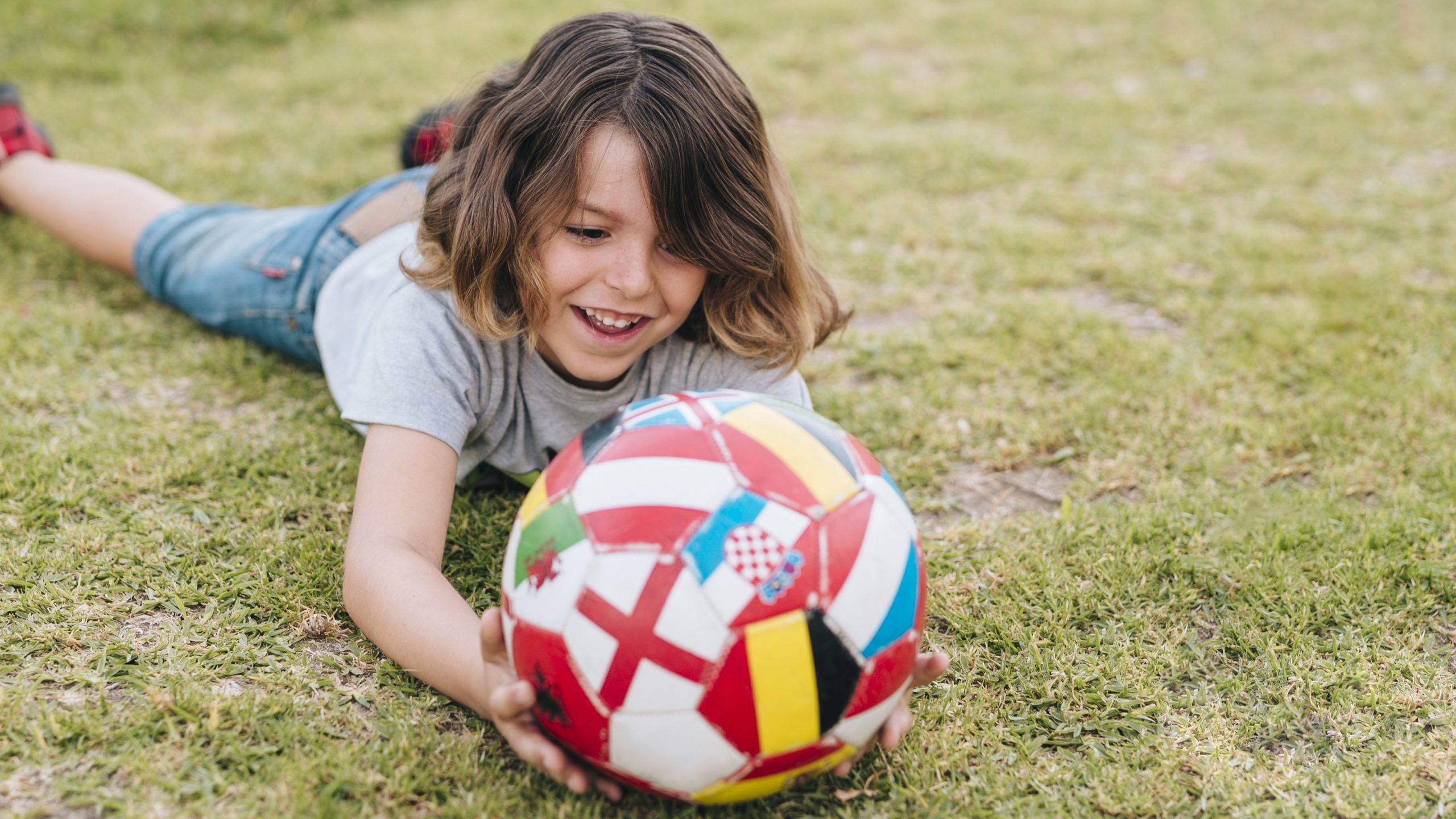 Ребенок валяется на лужайке на траве и держит в руках резиновый мяч
