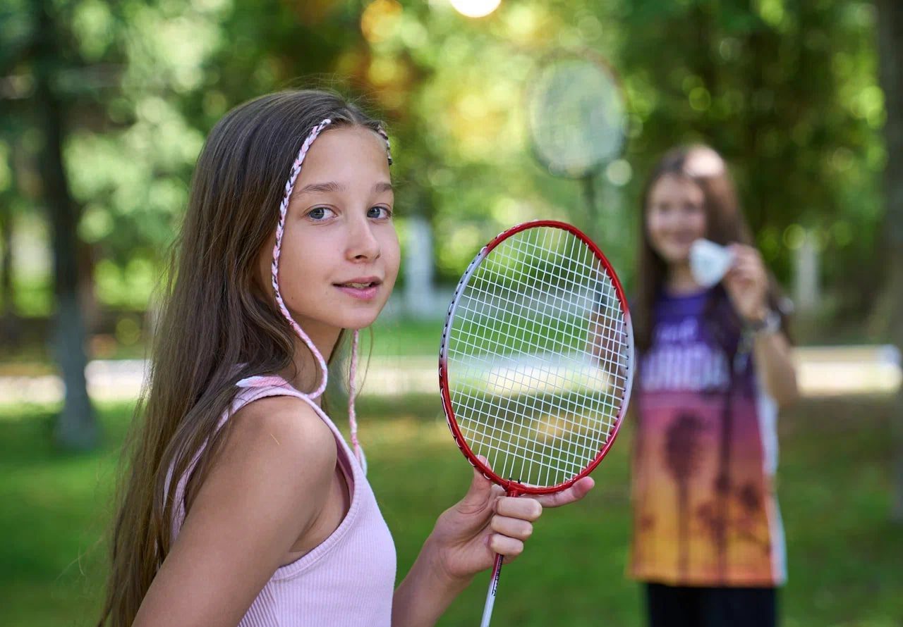 Две девочки в летнем лагере играют в бадминтон