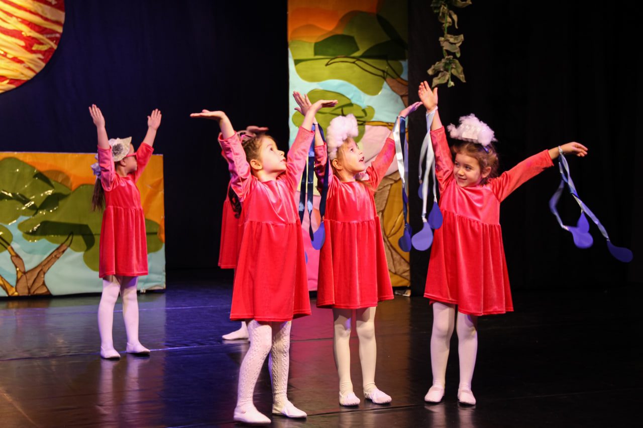 Маленькие девочки в красных платьях выступают на сене театра