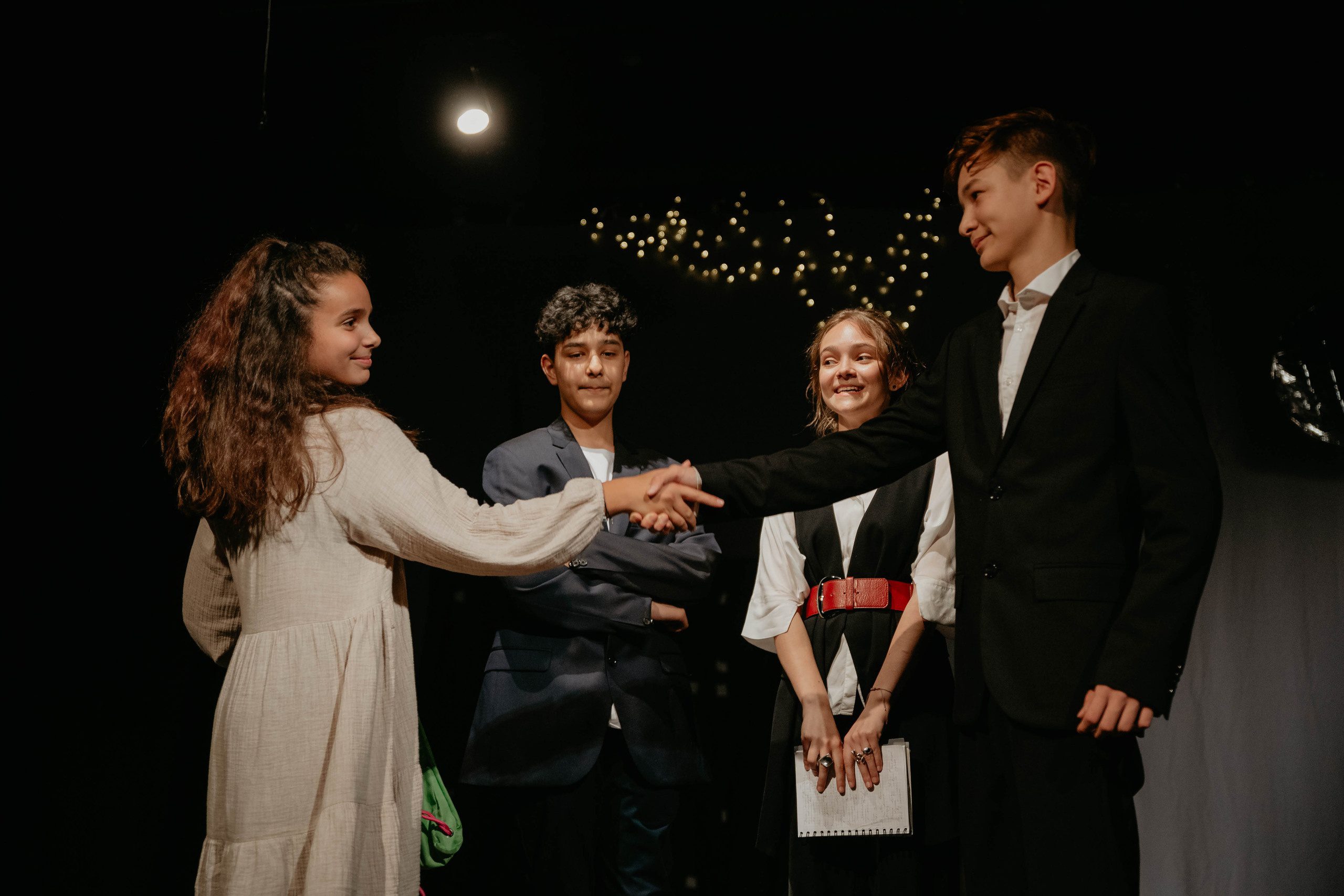 Подростки стоят на сцене разыгрывают номер из спектакля, где мальчик пожимает руку девочке