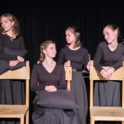 Девочки подростки в черных платьях ходят вокруг стульев разыгрывая сценку