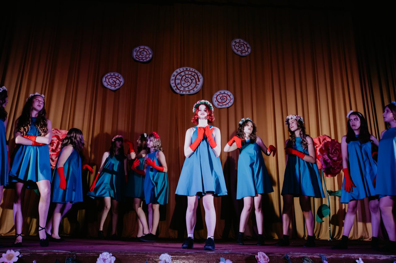 Девушки в голубых платьях и красных перчатках поют на сцене театра